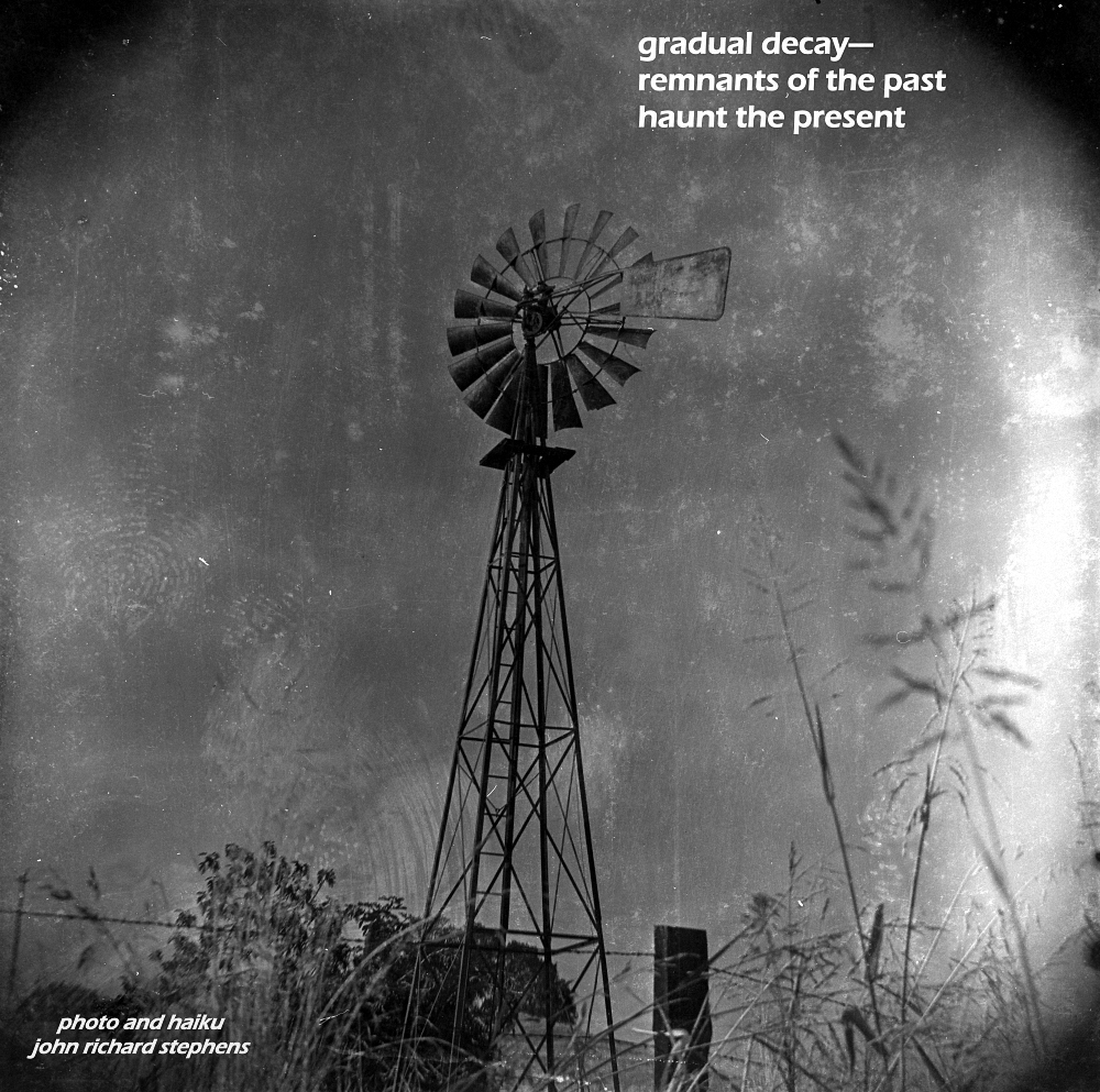 An old, degraded photograph of a windmill. A photo haiku with a black and white photograph of a very old windmill that had been used for drawing up water for cattle. The image is stained and degraded.